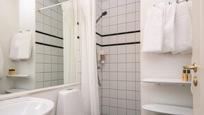 Een badkamer met toilet, wastafel en douche. Handdoeken hangen aan een rek en er is een spiegel boven de wastafel.