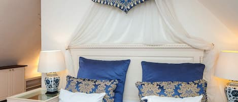 A bedroom with a canopy bed, white walls, and patterned bedding.