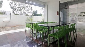 A covered outdoor dining area with a table and chairs, a ceiling fan, and a view of the outside. - Townhouse Financial District Gachibowli Formerly Srinika Inn (Hyderabad)