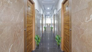 A hallway with marble walls, wooden doors, and potted plants. - Townhouse Financial District Gachibowli Formerly Srinika Inn (Hyderabad)