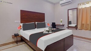 A hotel room with a large bed, bedside table with a phone and vase, a mirror, and an air conditioning unit on the wall. - Townhouse Financial District Gachibowli Formerly Srinika Inn (Hyderabad)