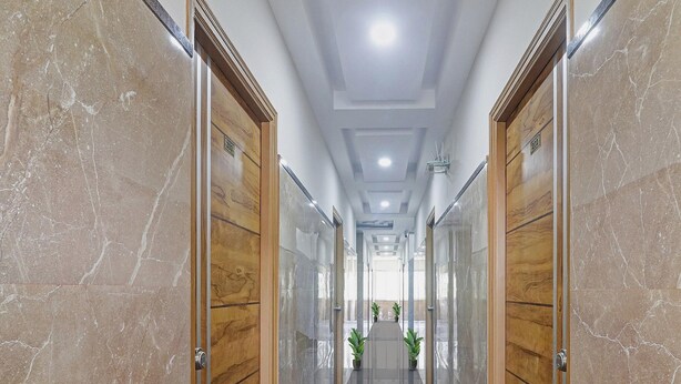 A hallway with marble walls, wooden doors, and potted plants. - Townhouse Financial District Gachibowli Formerly Srinika Inn (Hyderabad)
