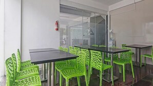 A conference room with a glass partition, green chairs, a black table, and a ceiling fan. - Townhouse Financial District Gachibowli Formerly Srinika Inn (Hyderabad)