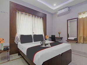 Camera d'albergo con un letto, un comodino con il telefono, uno specchio, una scrivania con una sedia e un condizionatore d'aria.