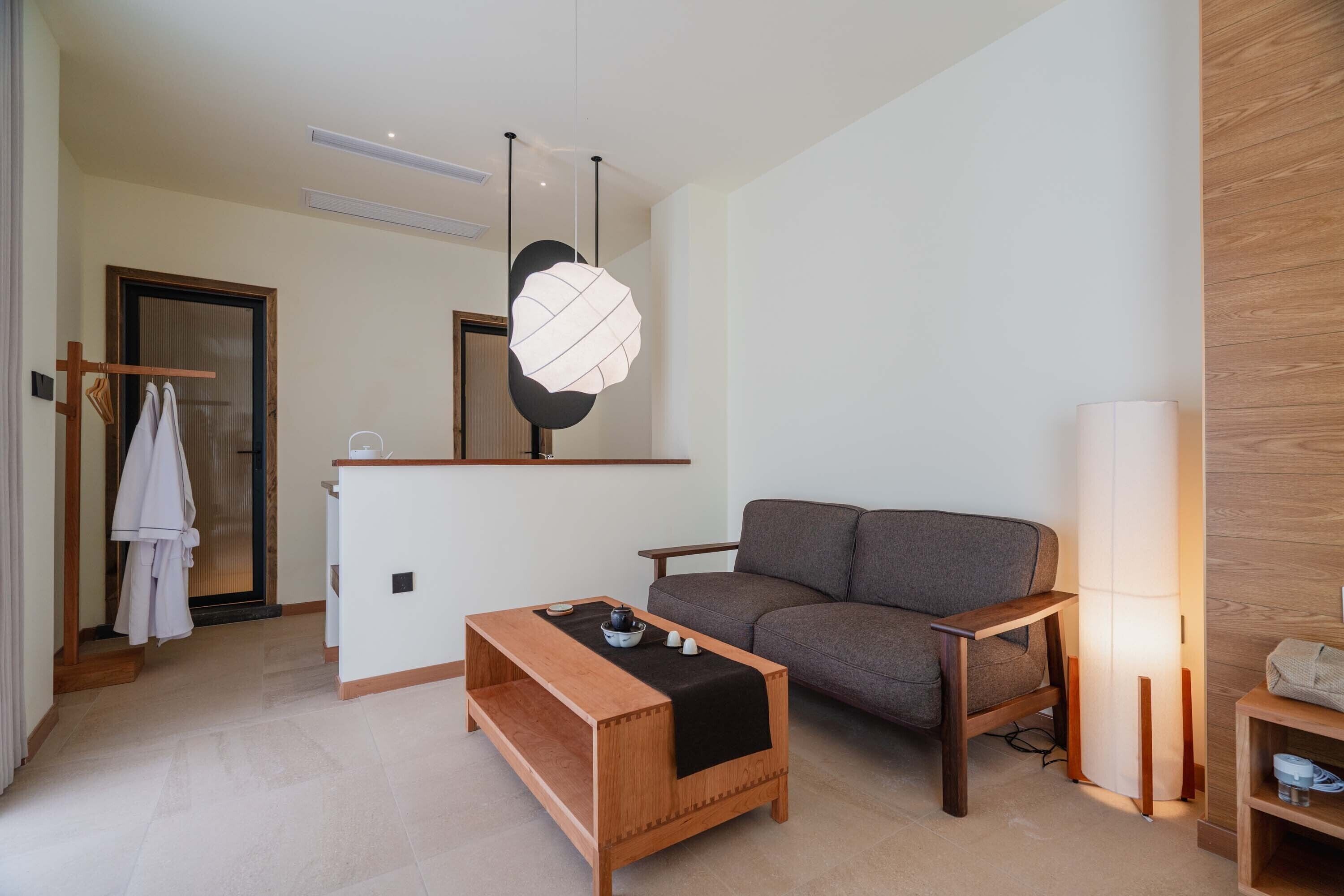 A modern living room with a sofa, a wooden coffee table, a hanging light fixture, and a standing lamp.