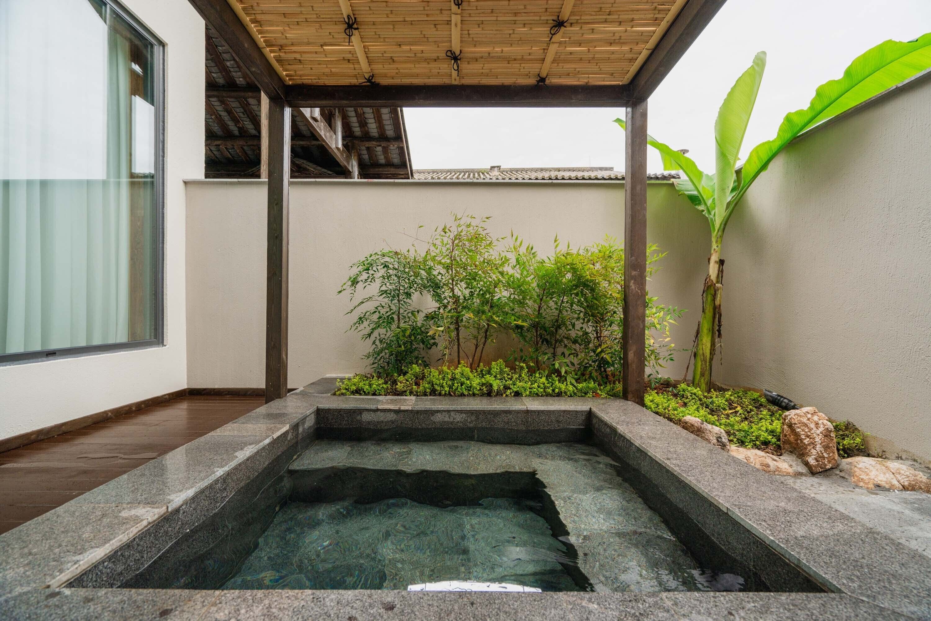 Ein Wellnessbereich mit Whirlpool, Holzterrasse und umliegender Bepflanzung.