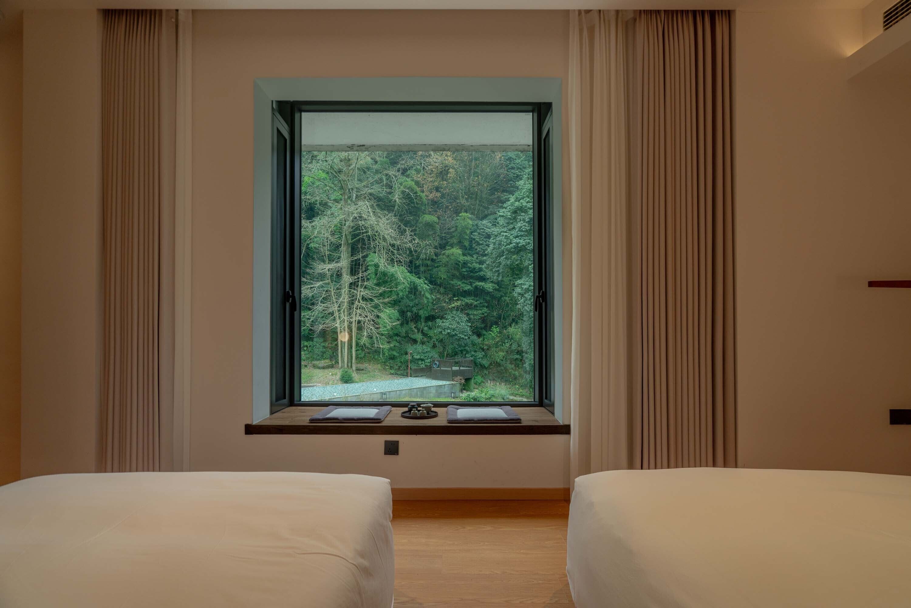 Une chambre avec deux lits, une grande fenêtre donnant sur une forêt et une petite table avec un plateau.