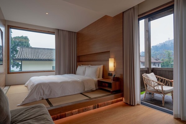 A modern hotel room with a large bed, a sitting area with a chair, and a view of a traditional building outside. - Emeishan XiaoshanQing Luxury Resort (Leshan)