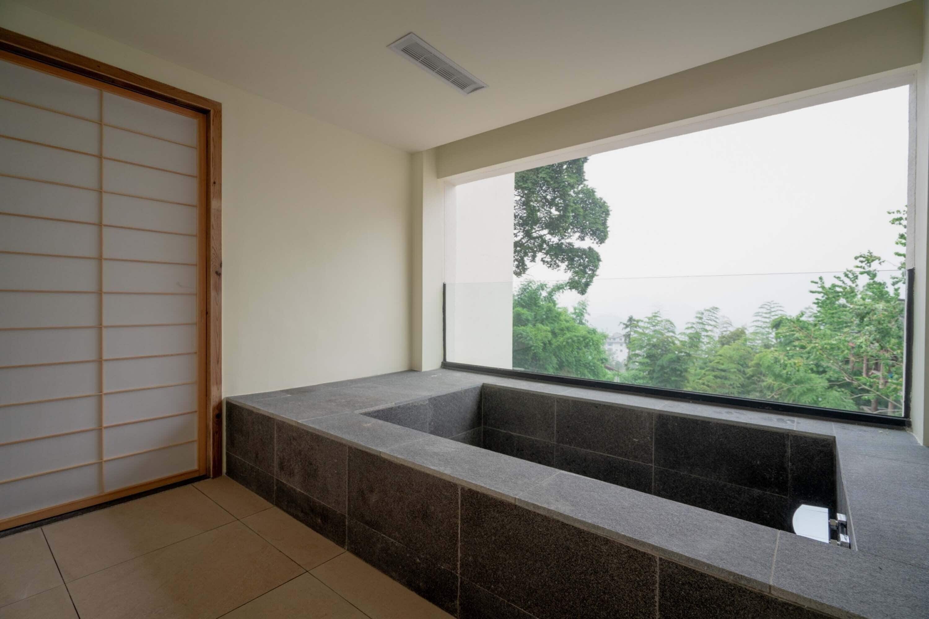 A modern bathroom with a large bathtub, a sliding shoji screen door, and a view of greenery outside.