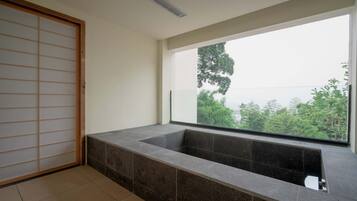 A modern bathroom with a large bathtub, a sliding shoji screen door, and a view of greenery outside.