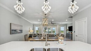 A modern kitchen with a large island, stainless steel sink, and white cabinetry. There are three pendant lights above the island and a ceiling fan. - New Listing! Lost Key Private Beach Club| 2 Swimming pools| Free Golf| Tennis| Bikes (Pensacola)