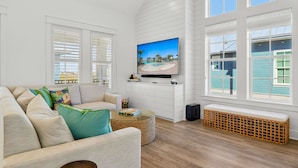 Ein modernes Wohnzimmer mit einem großen Flachbildfernseher, einem beigen Sofa, einem Korbtisch und einer Bank.