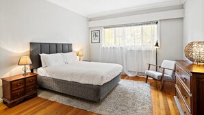 A bedroom with a bed, nightstands, a chair, a dresser, and a window with curtains. - Spacious 5-bed Home With Pool in Glen Iris (Melbourne)