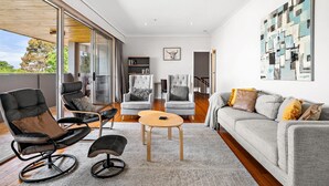 A modern living room with a grey sofa, two armchairs, a coffee table, and a bookshelf. - Spacious 5-bed Home With Pool in Glen Iris (Melbourne)