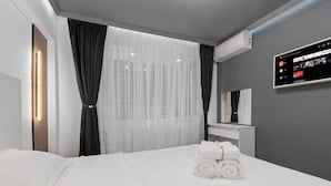 A modern hotel room with a neatly made bed, a flat-screen TV mounted on the wall, and a window with sheer curtains. - Apartament Lucas București  (Bucharest)