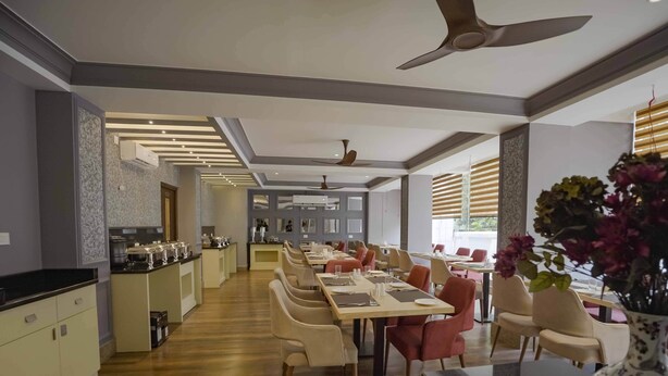 A modern dining area with a long table, chairs, and a kitchen in the background. - Meto Pema Hotel  (Phuntsholing)