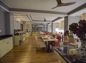 A modern dining area with a long table, chairs, and a kitchen in the background. - Meto Pema Hotel  (Phuntsholing)