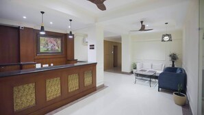 A reception area with a wooden counter, ceiling fans, pendant lights, a sofa, and a potted plant. - Meto Pema Hotel  (Phuntsholing)