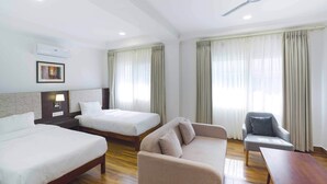 A hotel room with two beds, a sofa, a chair, a table, and a ceiling fan. - Meto Pema Hotel  (Phuntsholing)