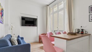 Una sala de estar moderna con un sofá azul, sillas rosadas, una mesa de comedor de madera y un televisor montado en la pared.