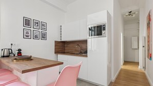 Una cocina moderna con armarios blancos, encimera de madera y una silla rosa.