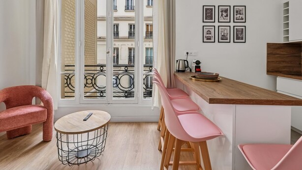 Una cocina moderna con encimera de madera, taburetes rosa y una mesa redonda con un control remoto.