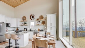 Et moderne køkken med hvide skabe, en stor ø med barstole og et spisebord dækket til seks personer.