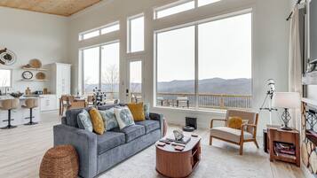 A spacious living room with a gray sofa, wooden coffee table, and a view of mountains through large windows.