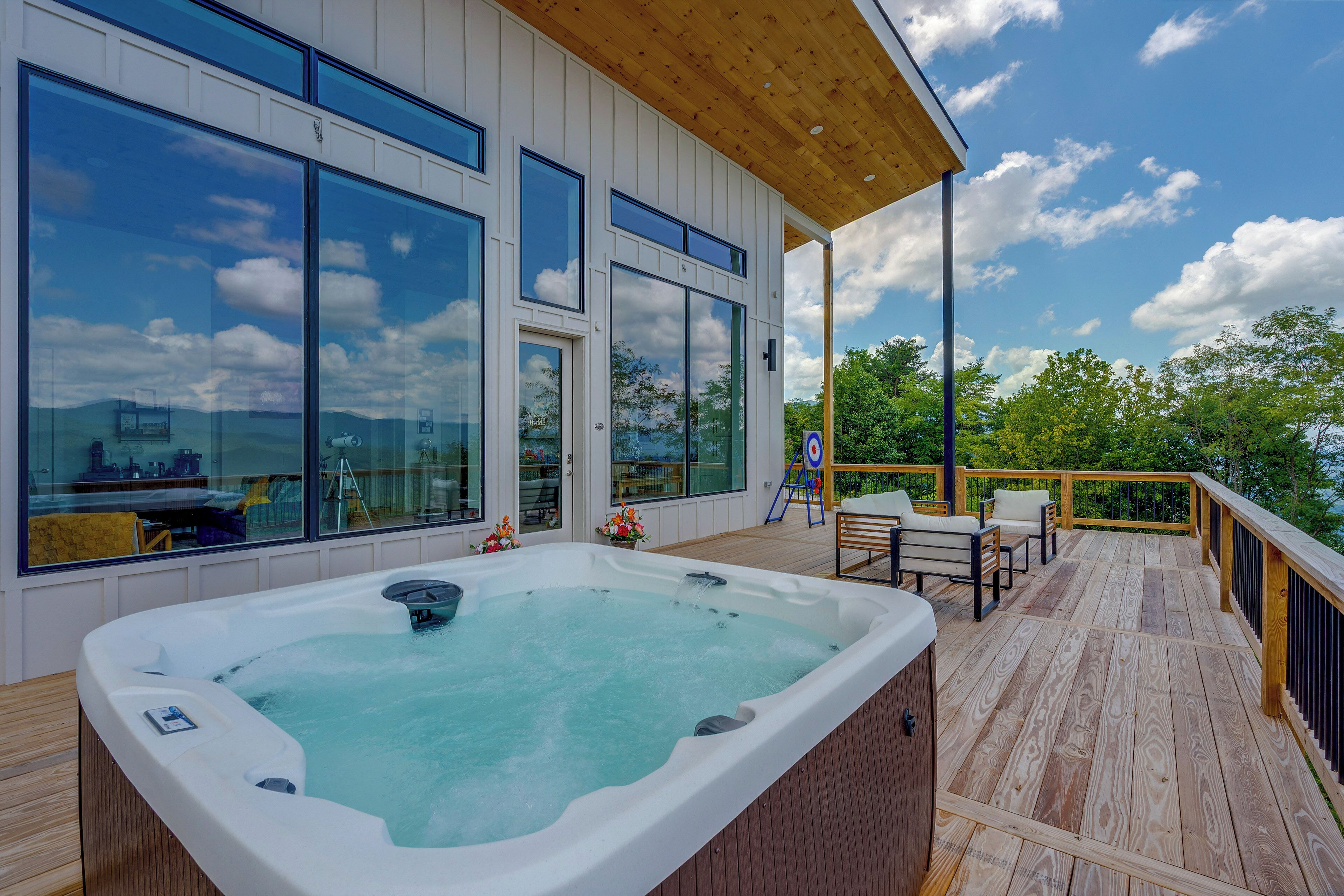 A hot tub on a wooden deck with large windows and a view of the sky.