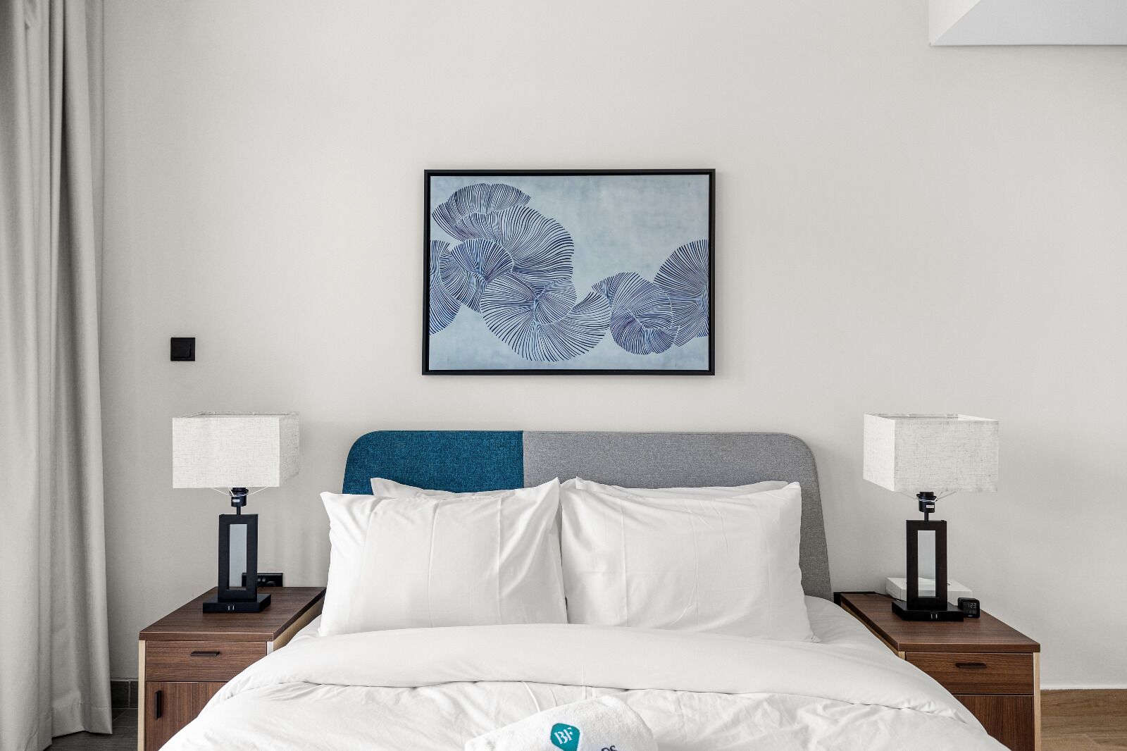 A neatly made bed with white linens, a blue and gray headboard, and two bedside lamps on wooden nightstands.