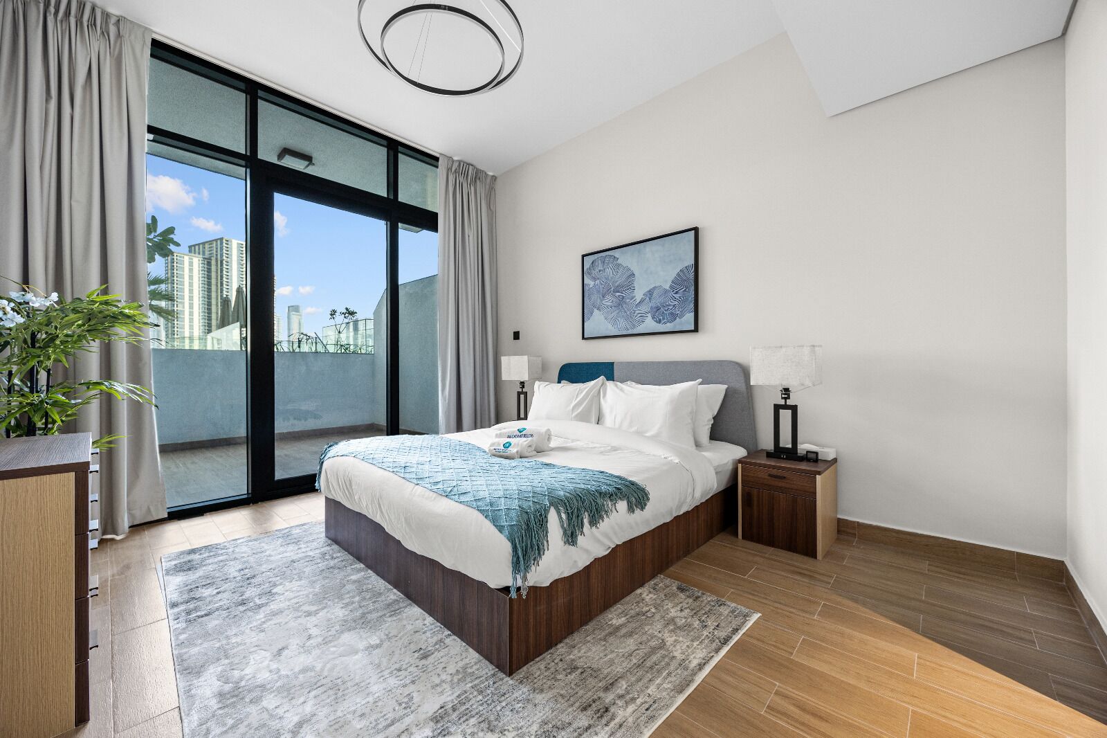 Ein modernes Schlafzimmer mit einem großen Bett, einem Nachttisch, einem Beistelltisch, einem Fenster mit Vorhängen und Blick auf die Stadt.