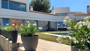 Una casa moderna con piscina, plantas en macetas y un muro de piedra.