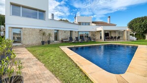 Una casa moderna con piscina, muros de piedra y un patio con mobiliario exterior.