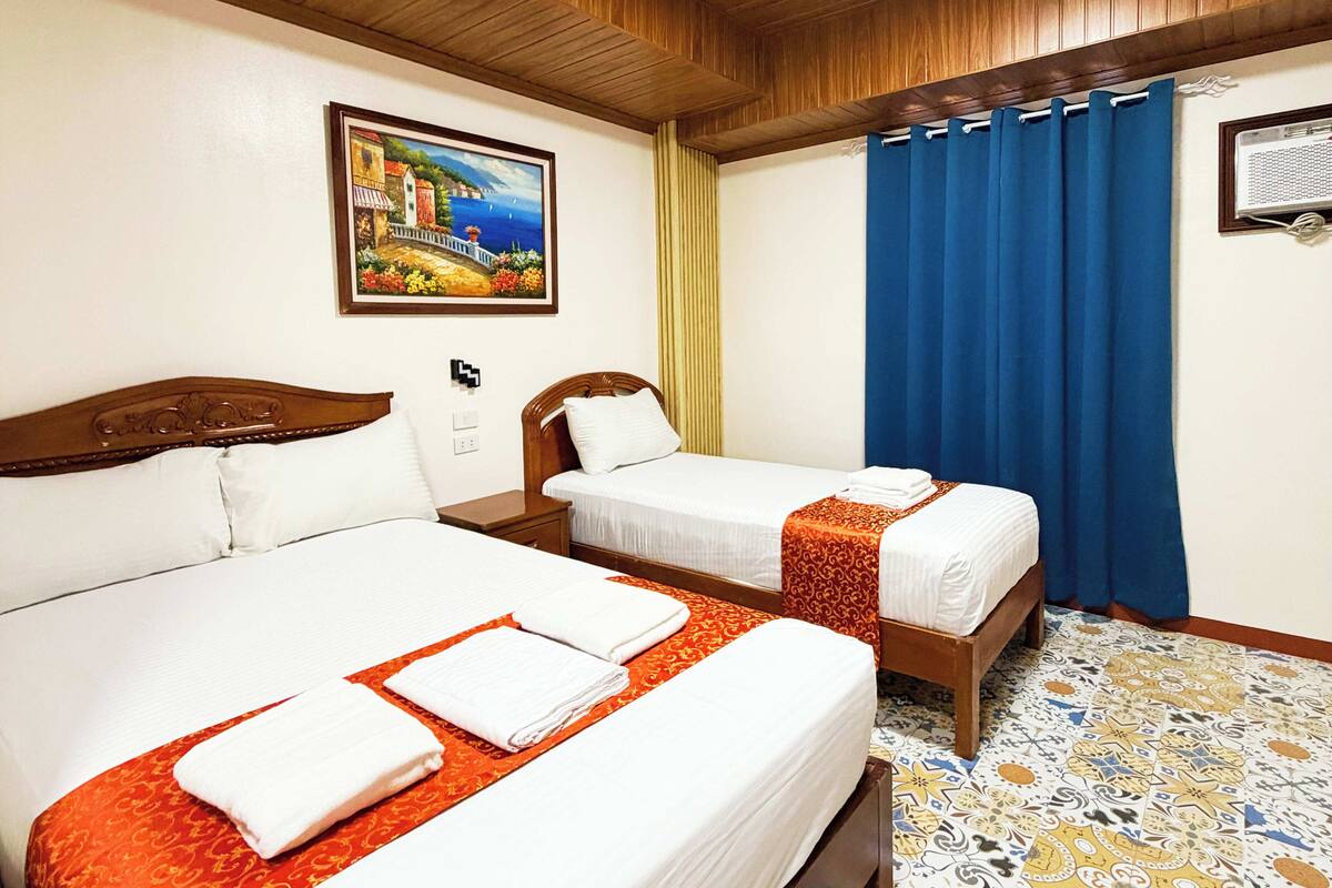 A hotel room with two beds, a painting on the wall, and a blue curtain.
