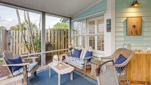 Un espace extérieur abrité, aménagé avec des meubles en osier et une table en bois, offrant une vue sur une clôture en bois et de la verdure.