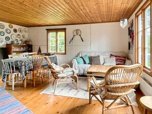 A cozy room with a wooden ceiling, a dining table with chairs, a sofa, and a window with a view of greenery. - 8 Person Holiday Home in Lottorp (Löttorp)