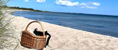 Une scène de plage avec un panier en osier et une couverture à rayures sur le sable.