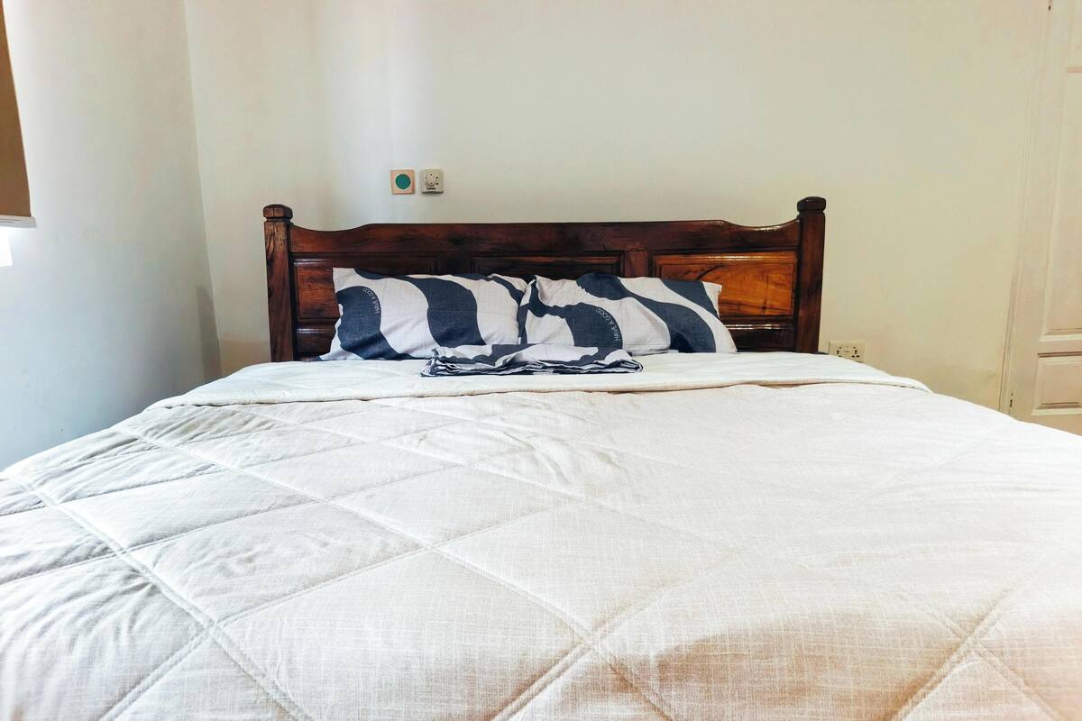 Una cama con edredón blanco acolchado, cabecera de madera y almohadas a rayas.