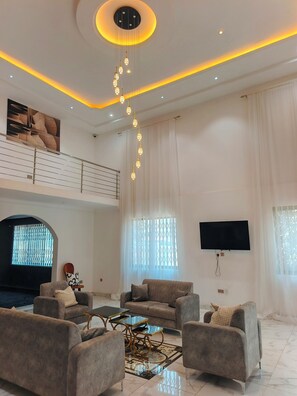 A spacious living room with a high ceiling, a large TV, and a fireplace. - JADA Hotel  (Prampram)