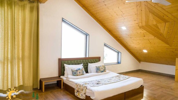 Ein Schlafzimmer mit schrägen Wänden, einem Bett mit grünem Kopfteil, zwei Fenstern und Holzboden.