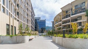 Une place urbaine moderne dotée d’un espace central ouvert, entourée d’immeubles à plusieurs étages, dotés de balcons et de grandes fenêtres.