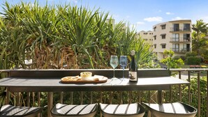 A balcony with a table set for two, featuring a bottle of wine, two glasses, and a bowl of olives.