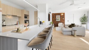 A modern kitchen with a central island, a dining area with a sofa and chairs, and a living room with a coffee table and a plant.