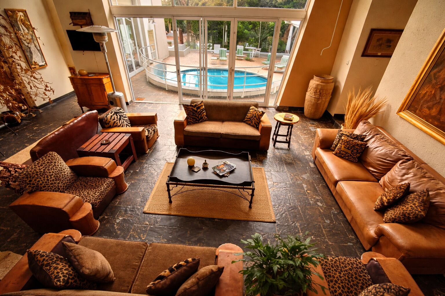 A spacious living room with leather sofas, a coffee table, and a view of a swimming pool through large windows.
