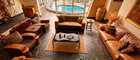 A spacious living room with leather sofas, a coffee table, and a view of a swimming pool through large windows.