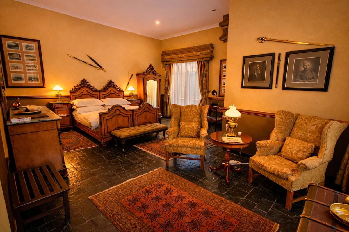 A hotel room with a bed, two armchairs, a small table, a desk, and a rug.
