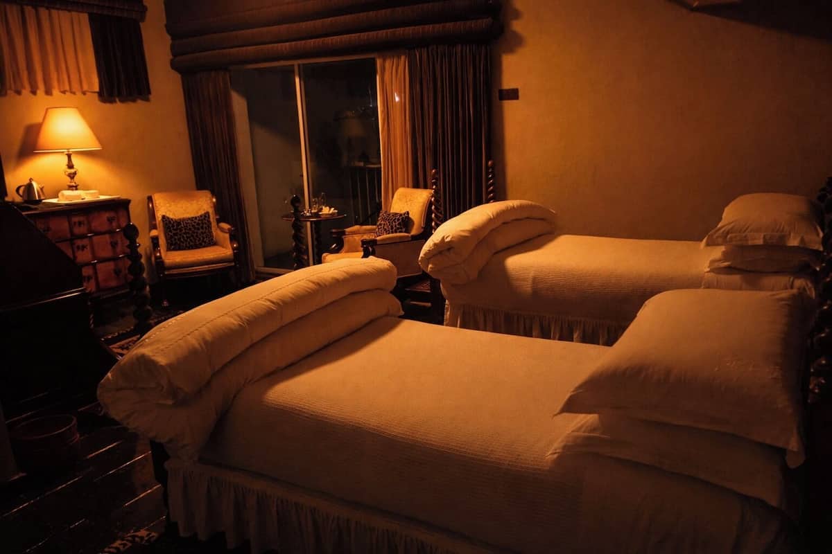 A hotel room with two beds, a lamp, a chair, and a small table.