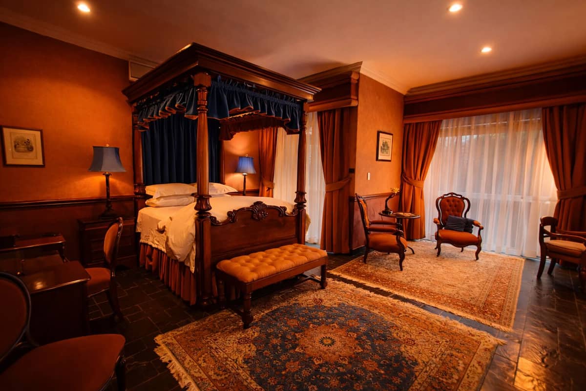A four-poster bed with a canopy, a sitting chair, a round table, and a bench.