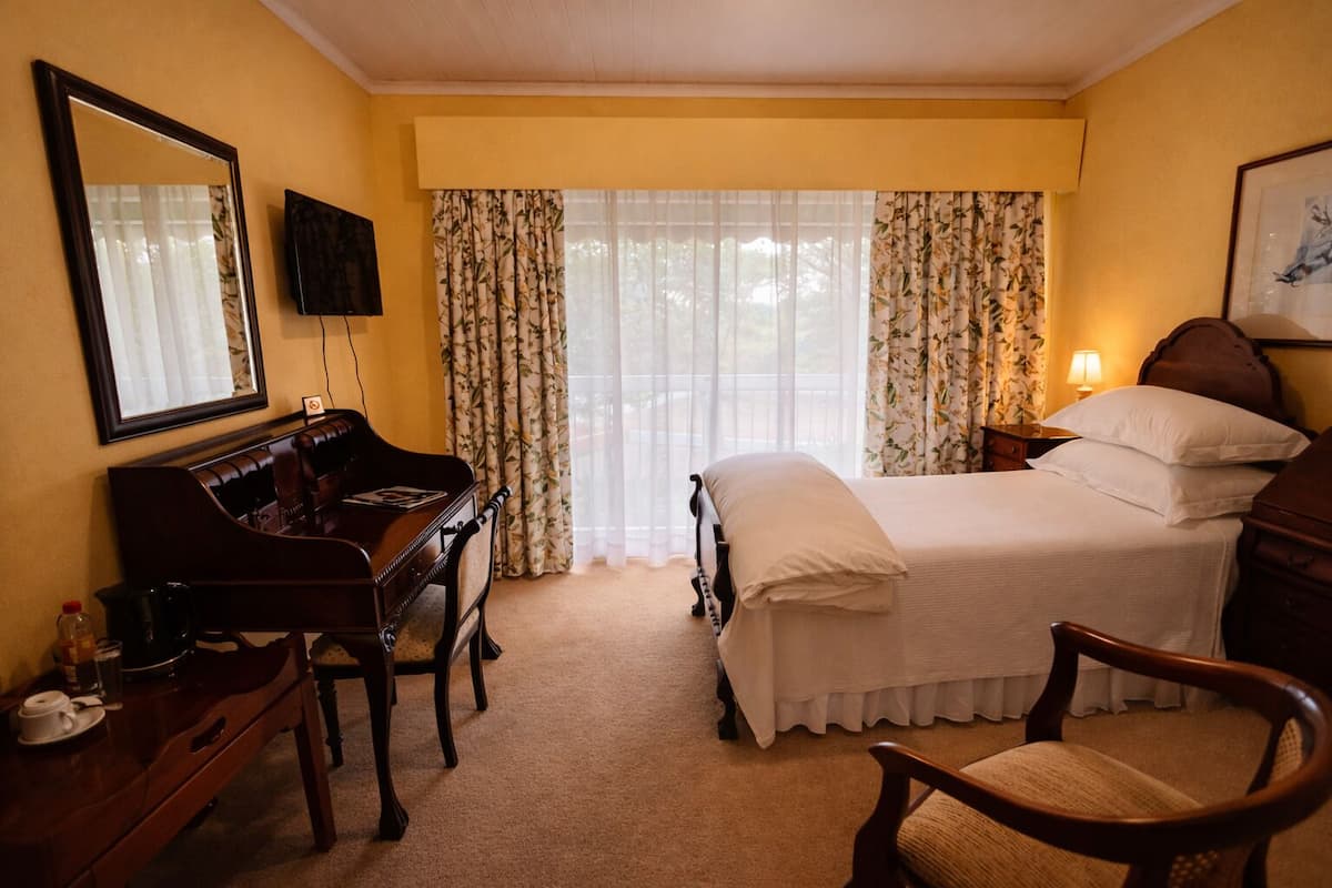 A hotel room with a bed, a desk with a piano, a chair, a TV, and curtains.