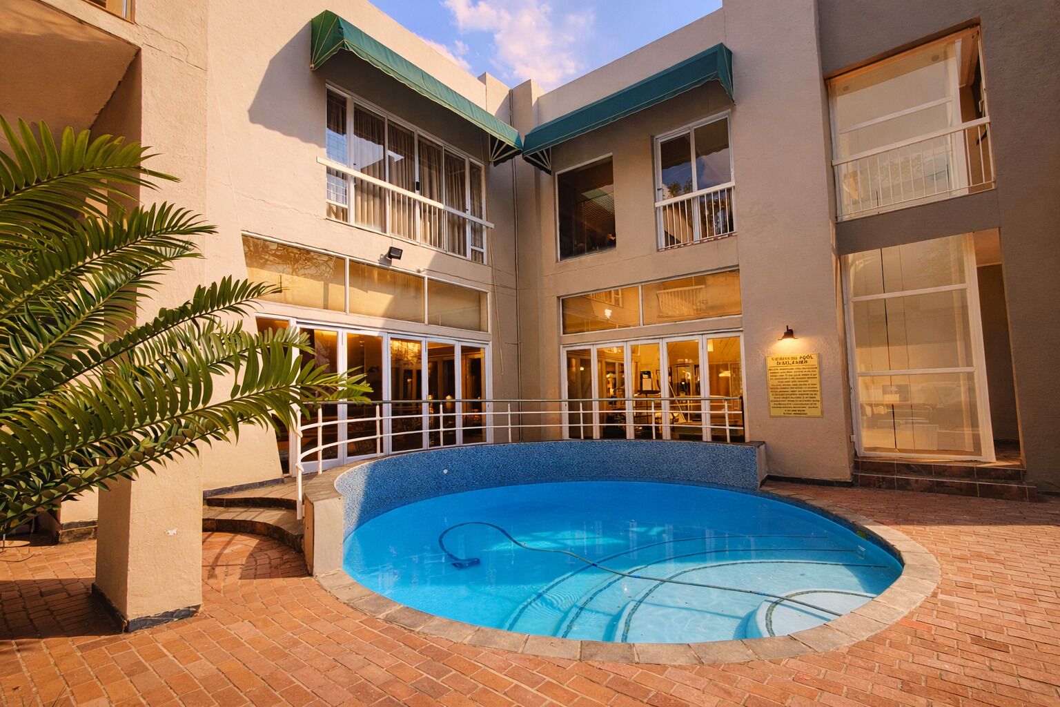 Un hotel con piscina central, varios balcones y un patio de ladrillo.